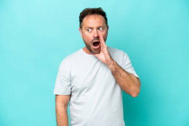 Mavi arka planda izole edilmiş orta yaşlı beyaz bir adam. Yan tarafa bakarken sürpriz bir jest yapıyor.