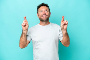 Middle age caucasian man isolated on blue background with fingers crossing and wishing the best