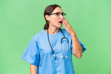 Orta yaşlı bir hemşire kadın izole edilmiş arka planda esniyor ve ağzını eliyle açık tutuyor.