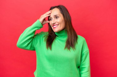 Orta yaşlı beyaz kadın, kırmızı arka planda izole edilmiş, gülümsüyor.