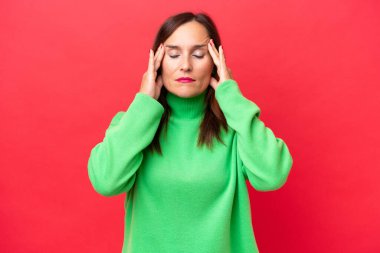 Orta yaşlı beyaz kadın, kırmızı arka planda izole edilmiş, baş ağrısı var.