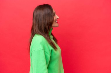 Orta yaşlı beyaz kadın, kırmızı arka planda yan pozisyonda izole edilmiş.