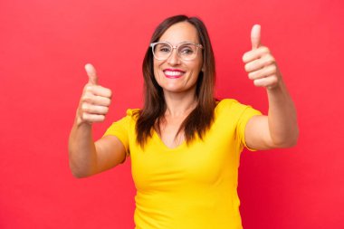 Kırmızı arka planda izole edilmiş orta yaşlı beyaz bir kadın baş parmak işareti yapıyor.