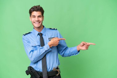 İzole edilmiş arka planda genç bir polis parmağı kenarı gösteriyor ve bir ürün sunuyor.