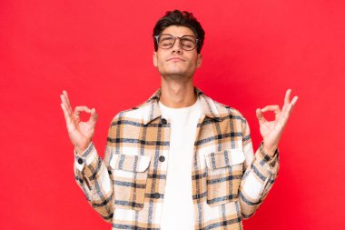 Zen pozisyonunda kırmızı arka planda izole edilmiş beyaz yakışıklı bir adam.