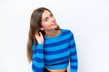 Beyaz arka planda izole edilmiş genç beyaz kadın elini kulağına koyarak bir şeyler dinliyor.