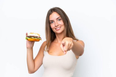 Beyaz arka planda izole edilmiş bir burger tutan genç ve güzel bir kadın kendinden emin bir ifadeyle seni işaret ediyor.