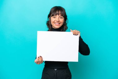 Mavi arka planda izole edilmiş genç Latin bir kadın elinde mutlu bir ifadeyle boş bir levha tutuyor.