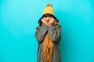 Mavi arka planda, kışlık ceket giyen genç Latin kadın.