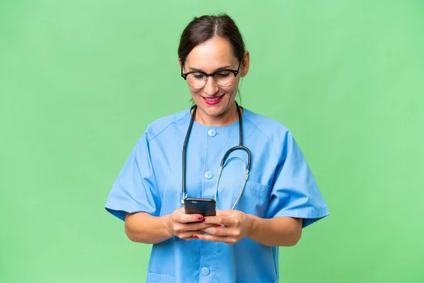 Enfermera Mediana Edad Sobre Antecedentes Aislados Enviando Mensaje Con Móvil —  Fotos de Stock