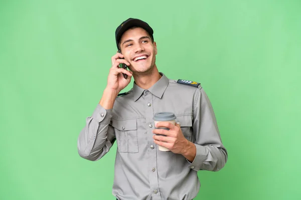 Young security man over isolated background holding coffee to take away and a mobile
