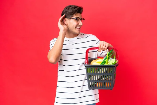 Mladý Běloch Muž Drží Nákupní Košík Plný Potravin Izolovaných Červeném — Stock fotografie