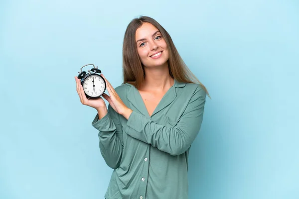 Jovem Bela Mulher Isolada Fundo Azul Pijama Segurando Relógio Com — Fotografia de Stock