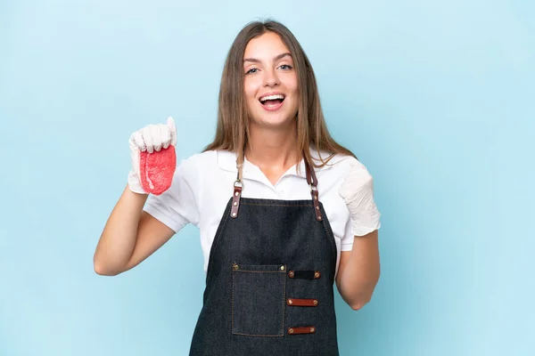 stock image Butcher caucasian woman wearing an apron and serving fresh cut meat isolated on blue background celebrating a victory in winner position