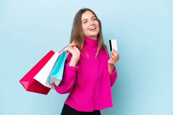 青の背景に隔離された若い美しい女性ショッピングバッグとクレジットカードを保持 — ストック写真