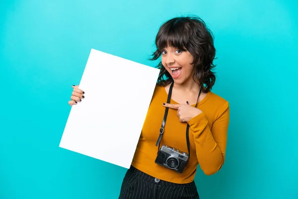 年轻的摄影师拉汀女士被隔离在蓝色的背景下 手里拿着一张空空的标语牌 脸上带着快乐的表情 并指着它 — 图库照片
