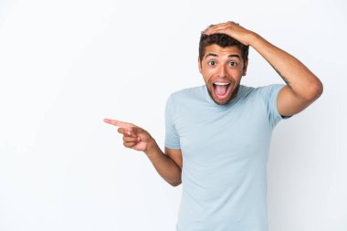 Beyaz arka planda izole edilmiş yakışıklı Brezilyalı bir adam şaşırmış ve parmağıyla kenarı işaret ediyor.