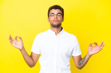 Genç yakışıklı Brezilyalı adam, sarı arka planda izole edilmiş, zen pozisyonunda.
