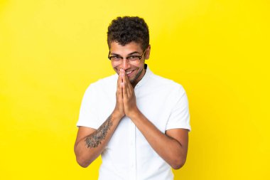Sarı arka planda izole edilmiş genç ve yakışıklı Brezilyalı adam avuç içlerini bir arada tutuyor. İnsan bir şey ister.