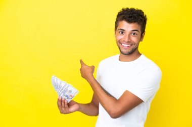 Genç Brezilyalı adam, sarı arka planda izole edilmiş bir sürü para alıyor.