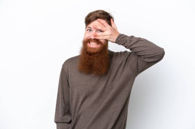 Kızıl saçlı, sakallı bir adam, beyaz arka planda izole edilmiş, gözleri elle kaplanmış ve gülümsüyor.