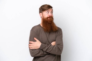 Beyaz arka planda sakallı kızıl saçlı bir adam omuzlarını kaldırırken şüpheyle hareket ediyor.