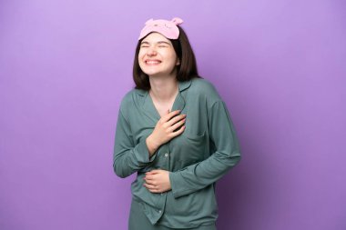 Young Russian woman in pajamas isolated on purple background smiling a lot