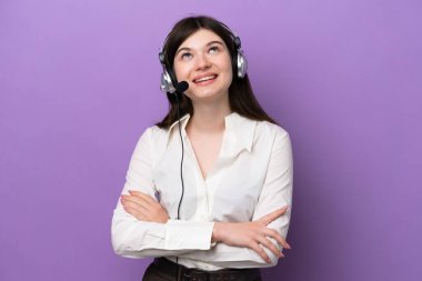 Mor arka planda izole edilmiş kulaklıkla çalışan pazarlamacı Rus kadın gülümserken yukarı bakıyor.