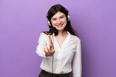 Mor arka planda izole edilmiş bir kulaklıkla çalışan pazarlamacı Rus kadın parmağını kaldırıyor ve gösteriyor.