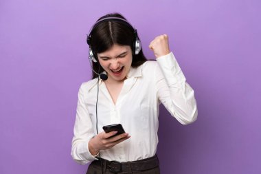 Mor arka planda izole edilmiş kulaklıkla çalışan pazarlamacı Rus kadın zafer pozisyonunda telefonla konuşuyor.