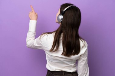 Mor arka planda izole edilmiş kulaklıkla çalışan pazarlamacı Rus kadın işaret parmağıyla işaret ediyor.