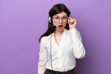 Mor arka planda gözlüklü ve şaşırmış bir kulaklıkla çalışan pazarlamacı Rus kadın.