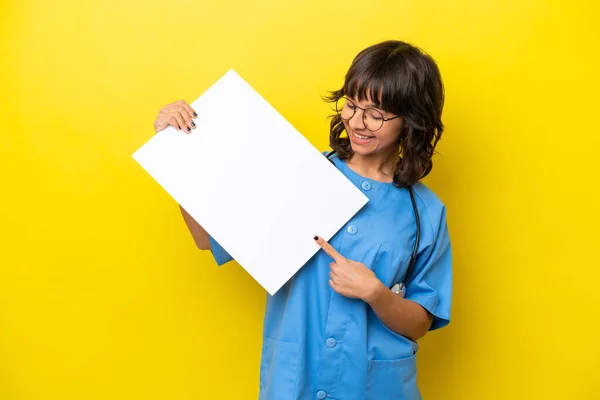 年轻的护士医生女士 黄底孤零零地举着一张空空的标语牌 满脸喜色 指点着它 — 图库照片