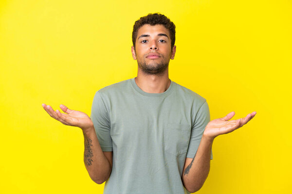 Young handsome Brazilian man isolated on yellow background having doubts