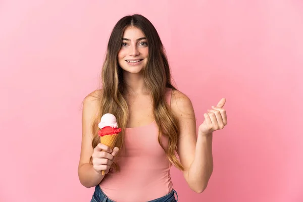 若いですCaucasian女性とともにCornetアイスクリーム孤立オンピンク背景作るお金ジェスチャー — ストック写真