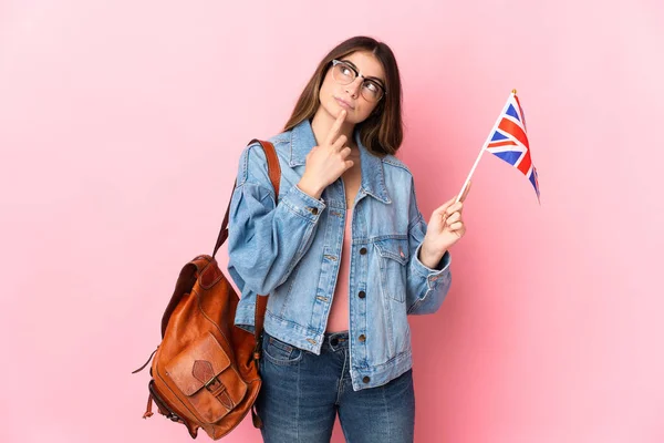举着英国国旗的年轻女子 背景为粉色 在仰视时感到疑惑 — 图库照片