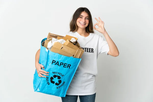 リサイクルバッグを持っている若い女性は 指でOkサインを示す白い背景に隔離されたリサイクルするために紙でいっぱい — ストック写真