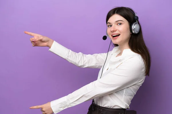 テレマーケティング担当者ロシアの女性は 紫色の背景に指差す指でヘッドセットで作業し 製品を提示 — ストック写真