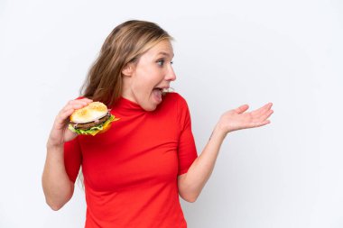 Beyaz arka planda yüzü sürpriz bir şekilde izole edilmiş bir burger tutan genç sarışın kadın.