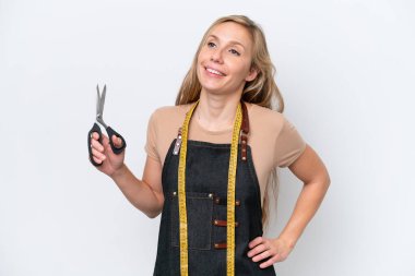 Beyaz arka planda soyutlanmış genç sarışın terzi kadın kolları kalçasında ve gülümsüyor.
