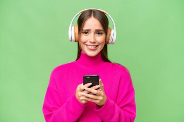 Genç, güzel, beyaz bir kadın izole edilmiş arka planda müzik dinliyor ve ön tarafa bakıyor.