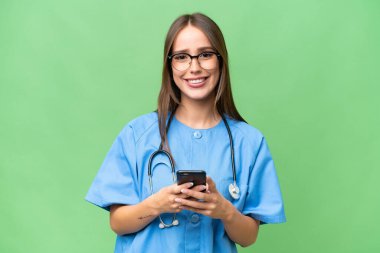 Genç beyaz kadın, izole edilmiş arka planda cep telefonuyla mesaj yolluyor.