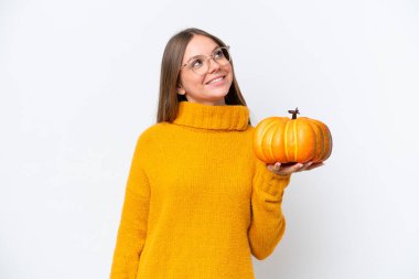 Beyaz arka planda izole edilmiş balkabağı tutan beyaz bir kadın gülümserken yukarı bakıyor.