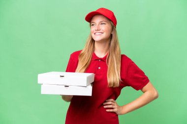 İş üniformalı, beyaz pizza dağıtan genç bir kadın izole arka planda pizza kutularını alıyor. Kolları kalçasında ve gülümsüyor.