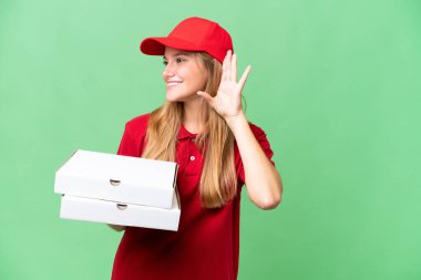 İş üniformalı beyaz bir kadın izole edilmiş arka planda pizza kutularını topluyor. Kulağına elini sürerek bir şeyler dinliyor.