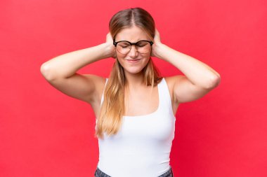 Kızıl arka planda izole edilmiş genç bir kadın hayal kırıklığına uğramış ve kulaklarını kapatmış.