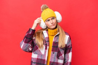 Young beautiful woman wearing winter muffs isolated on red background having doubts and with confuse face expression clipart