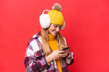 Kırmızı arka planda izole edilmiş kışlık kuklalar takan güzel bir kadın cep telefonuyla mesaj yolluyor.