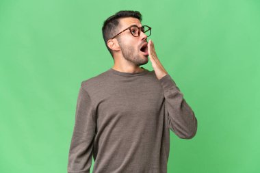 Genç, yakışıklı, beyaz bir adam izole edilmiş arka planda esniyor ve ağzını eliyle kapatıyor.