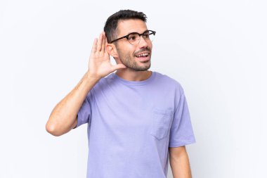 Beyaz arka planda izole edilmiş genç beyaz bir adam. Kulağına elini sürerek bir şeyler dinliyor.